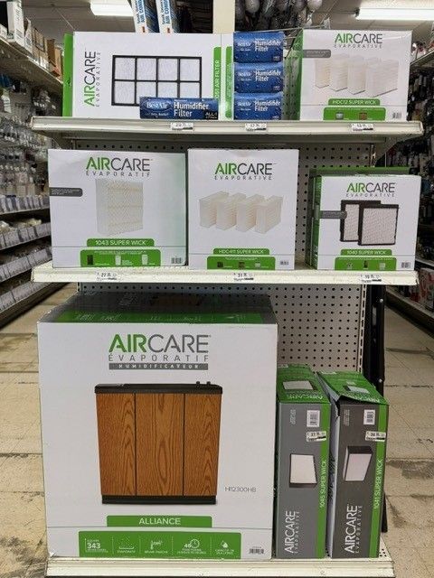 Shelves displaying various AirCare air purifier products in a store setting. Boxes in white and green.