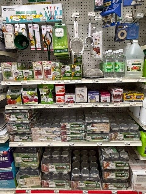 Shelf stocked with canning jars, supplies, and food processing tools in a store setting.