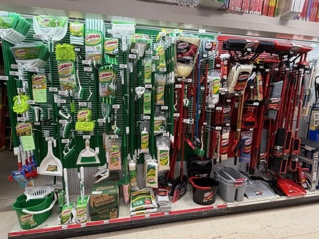 Cleaning supplies display in a store; various brooms, mops, sponges, and cleaning products are arranged on shelves.