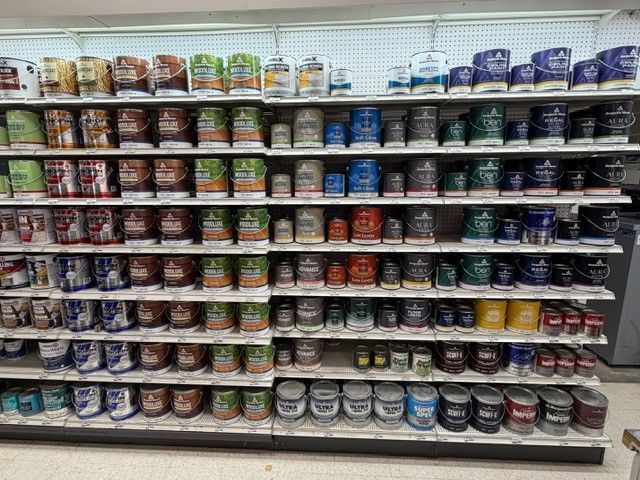Shelves stocked with various paint cans, arranged by color in a store.
