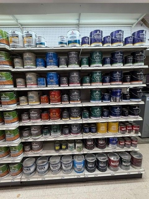 Shelves stocked with various paint cans, arranged by color, in a store setting.