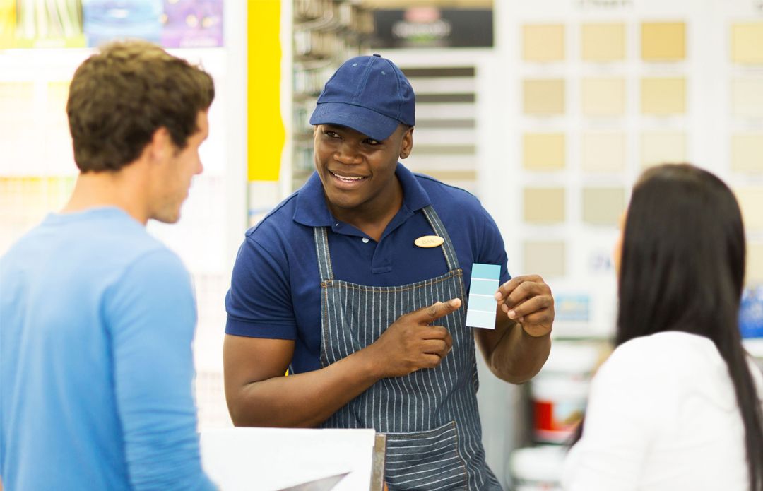 A man in an apron is talking to two customers in a store.
