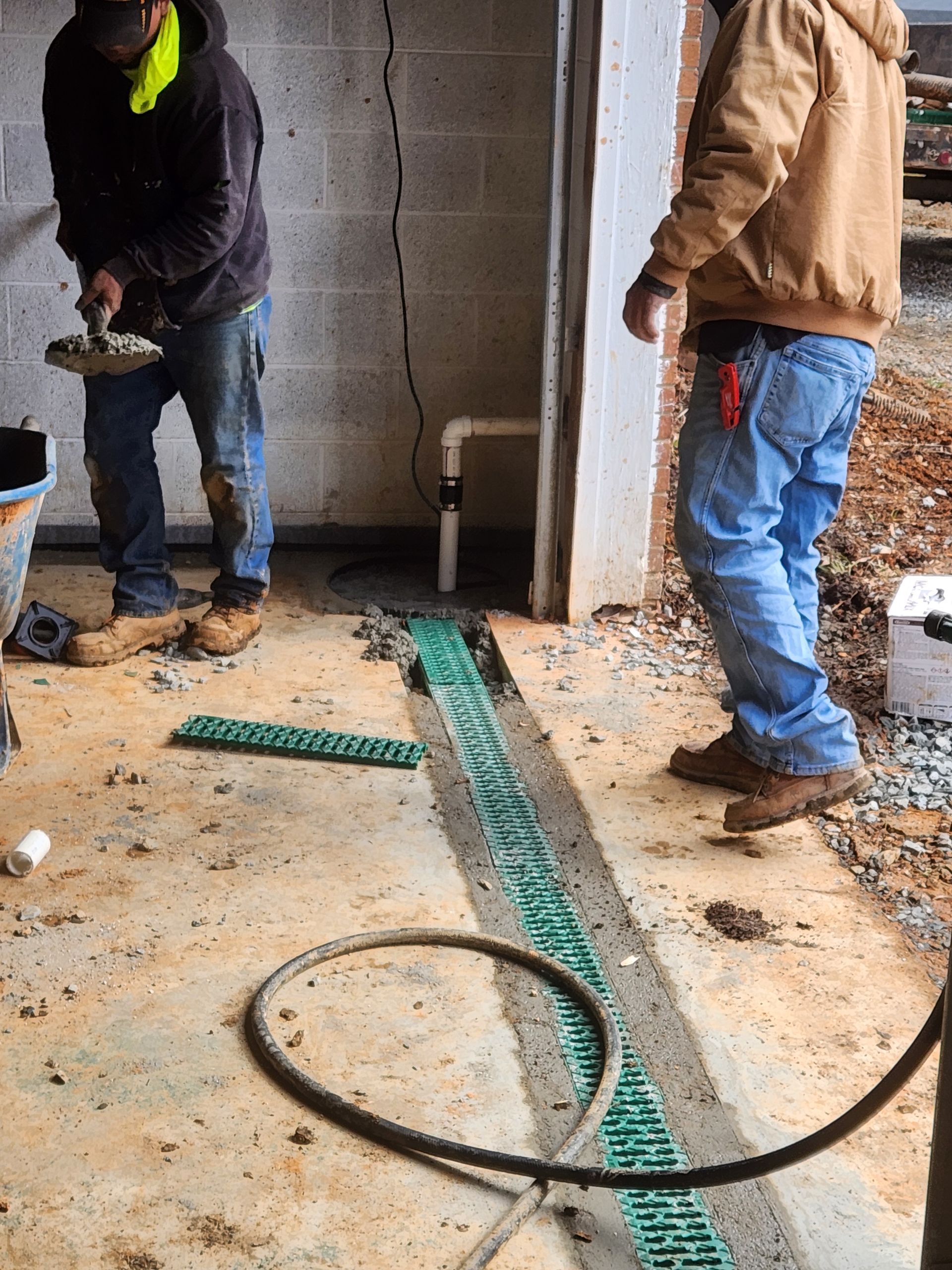 Two men are working on a drainage system in a basement