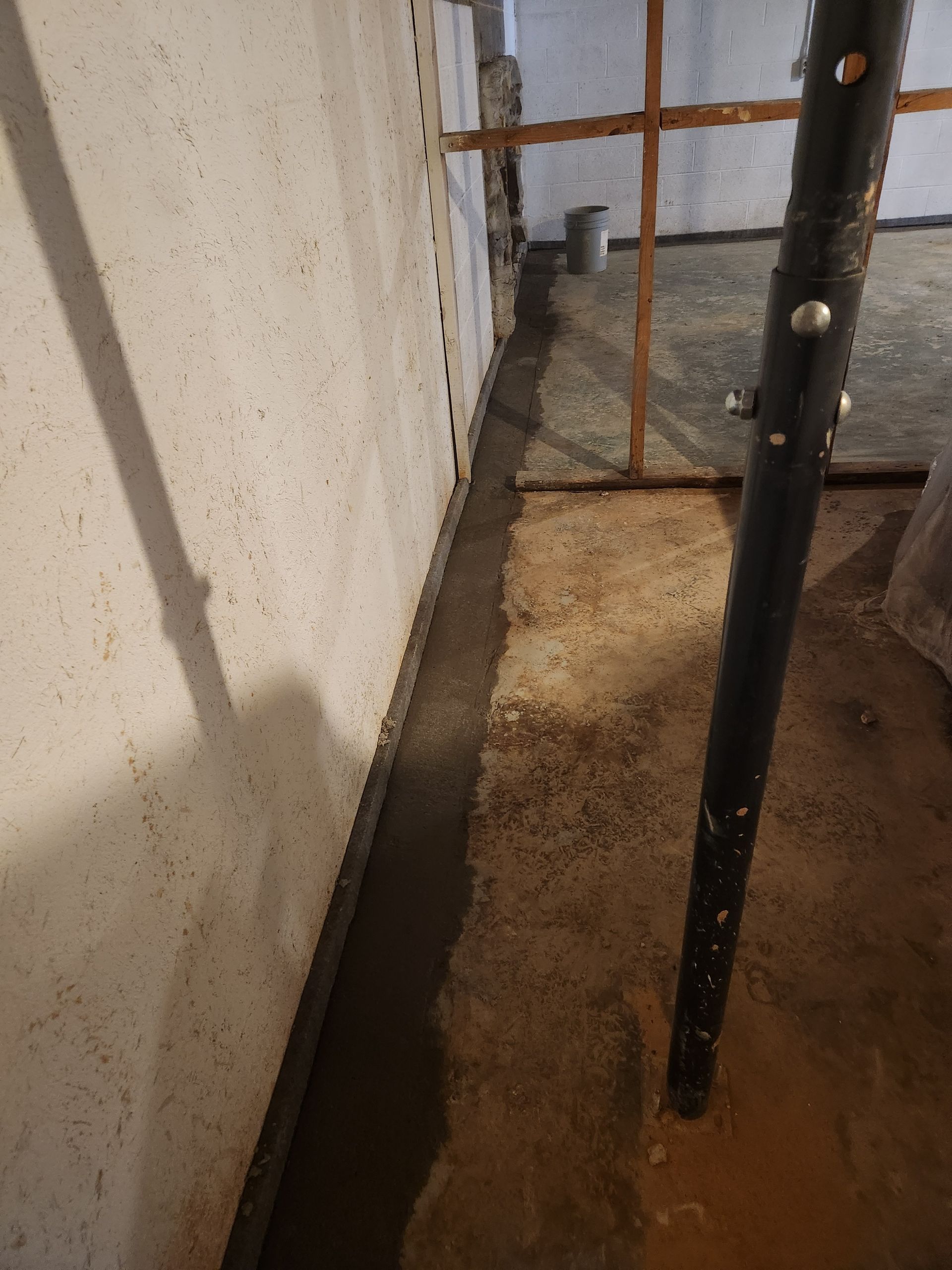 A black pole is sitting next to a wall in a basement.