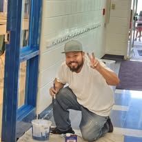 A man is kneeling down and painting a wall in a hallway.
