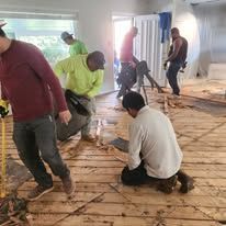 A group of men are working on a wooden floor in a room.