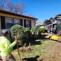 A man is standing in front of a house holding a shovel.