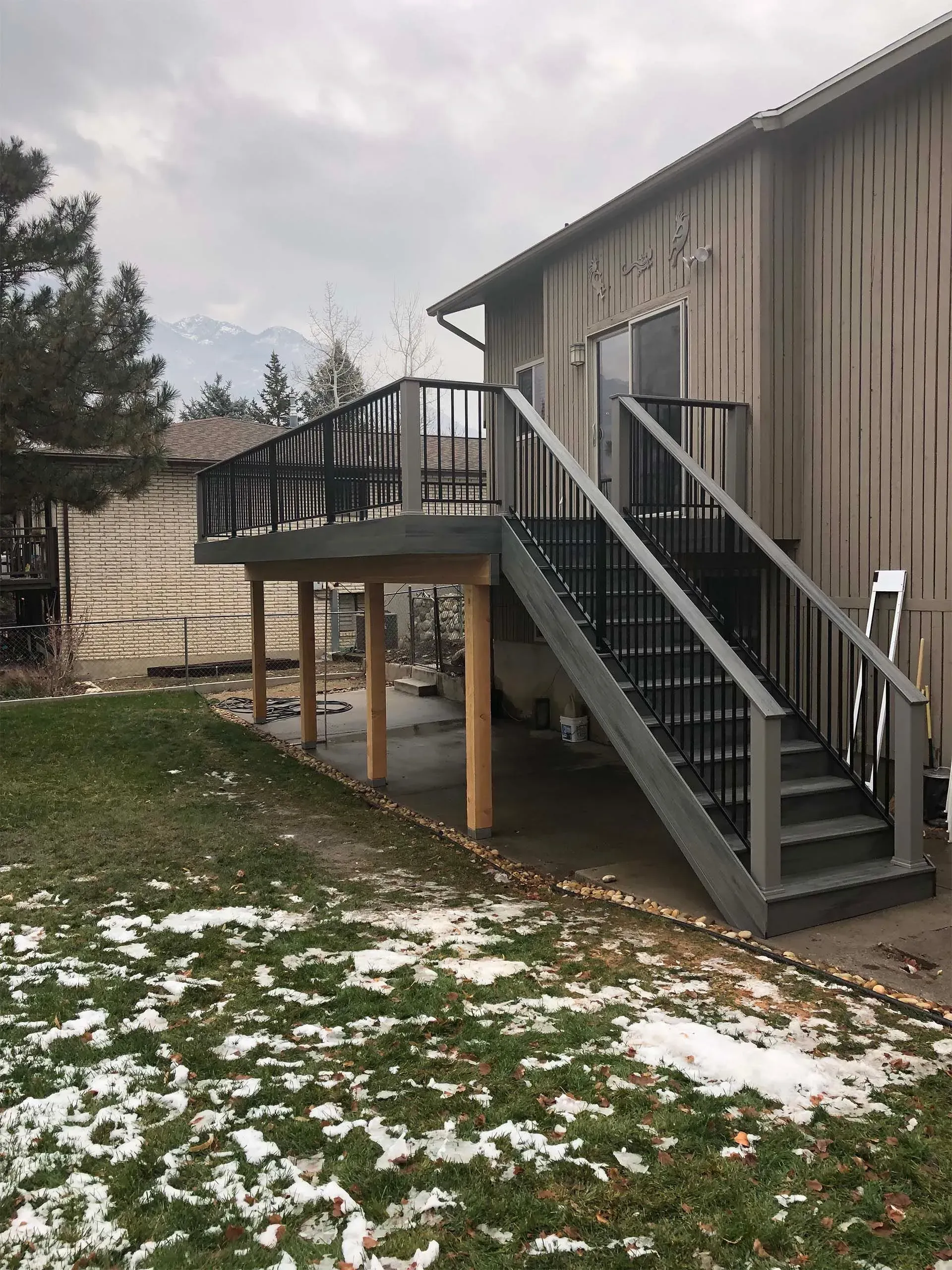 A wooden deck with black railings and stairs attached to a house, on a grassy yard.