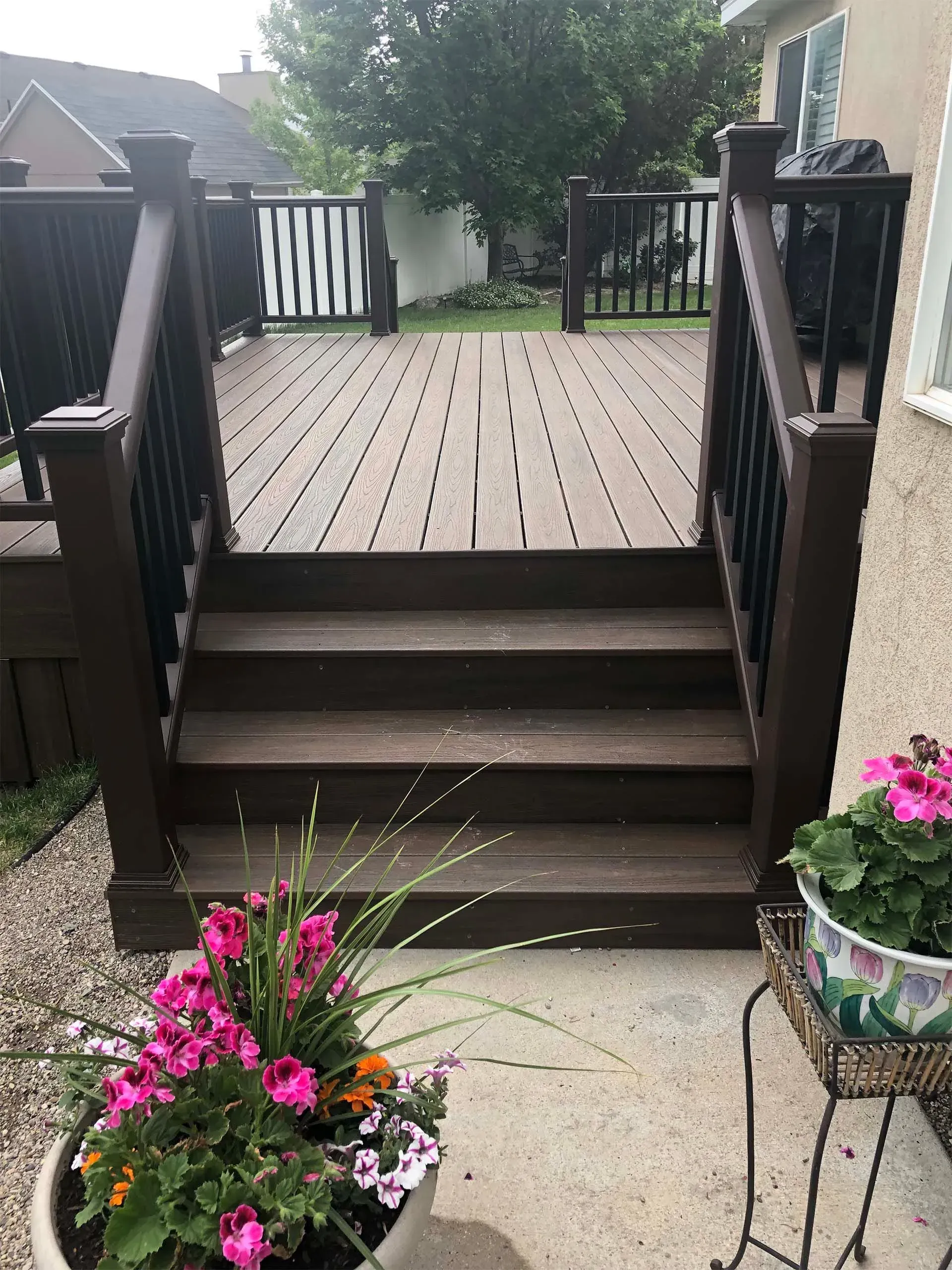 Wooden deck with steps, dark brown railing, and colorful potted flowers.