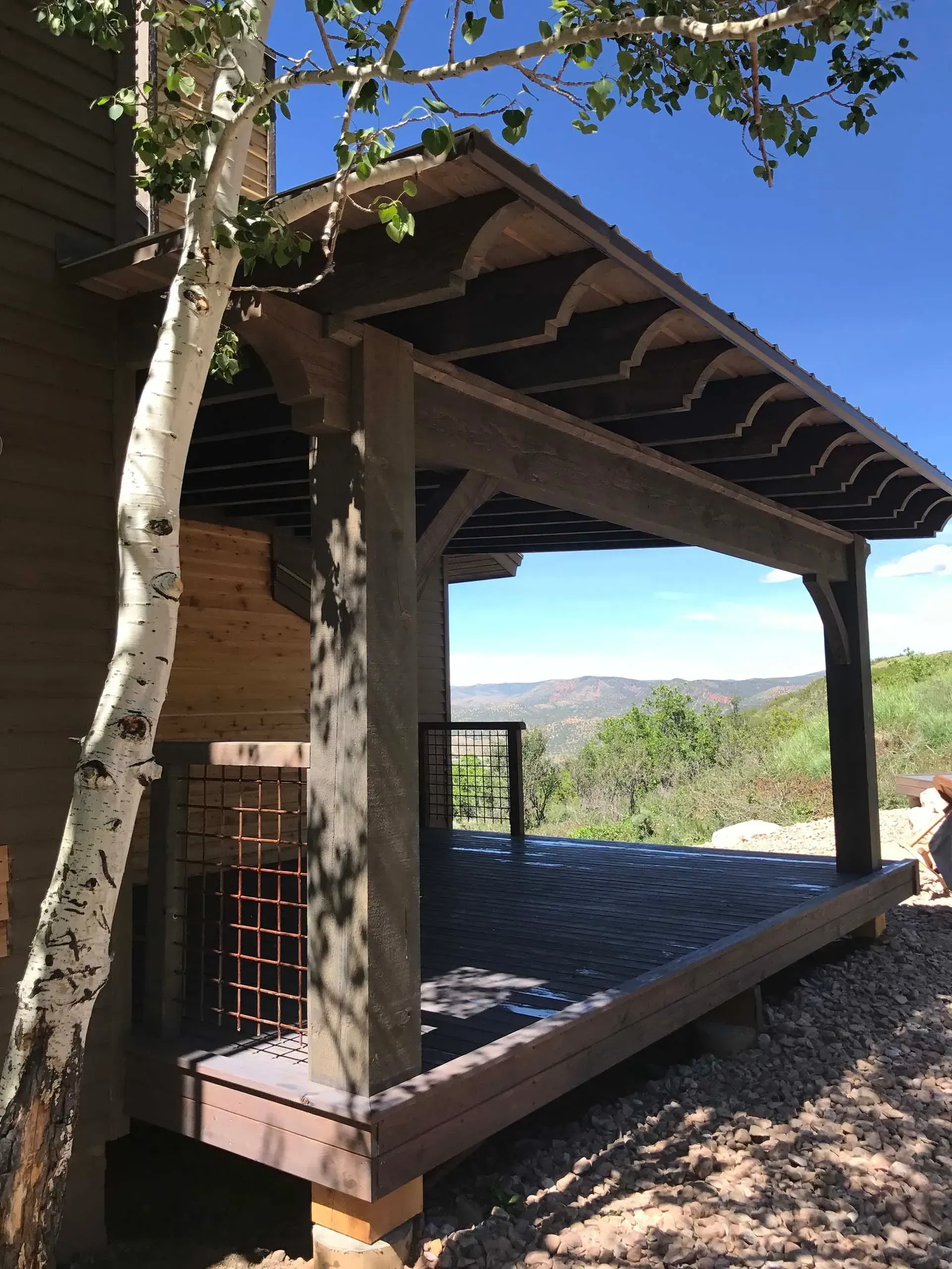 Covered outdoor deck with dark wood, overlooking a mountain view on a sunny day.
