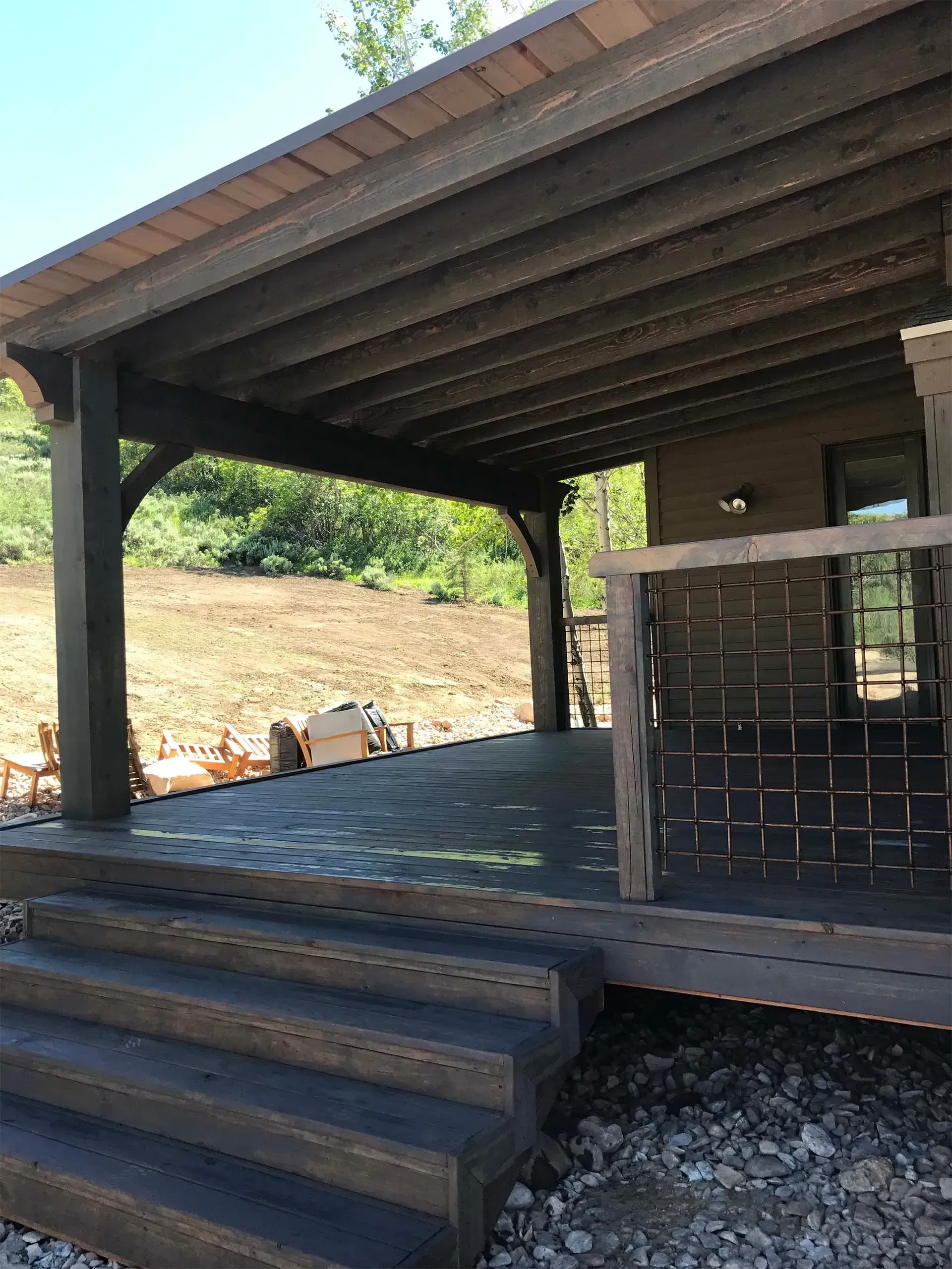 Covered wooden deck with steps, gray-brown color, and a view of a hillside.