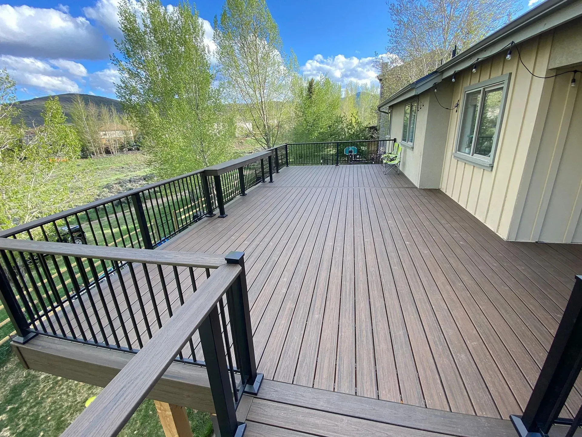 Large wooden deck with black railing, overlooking a green landscape.