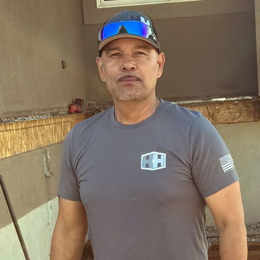 A man wearing a cap and a gray shirt stands outside a building.