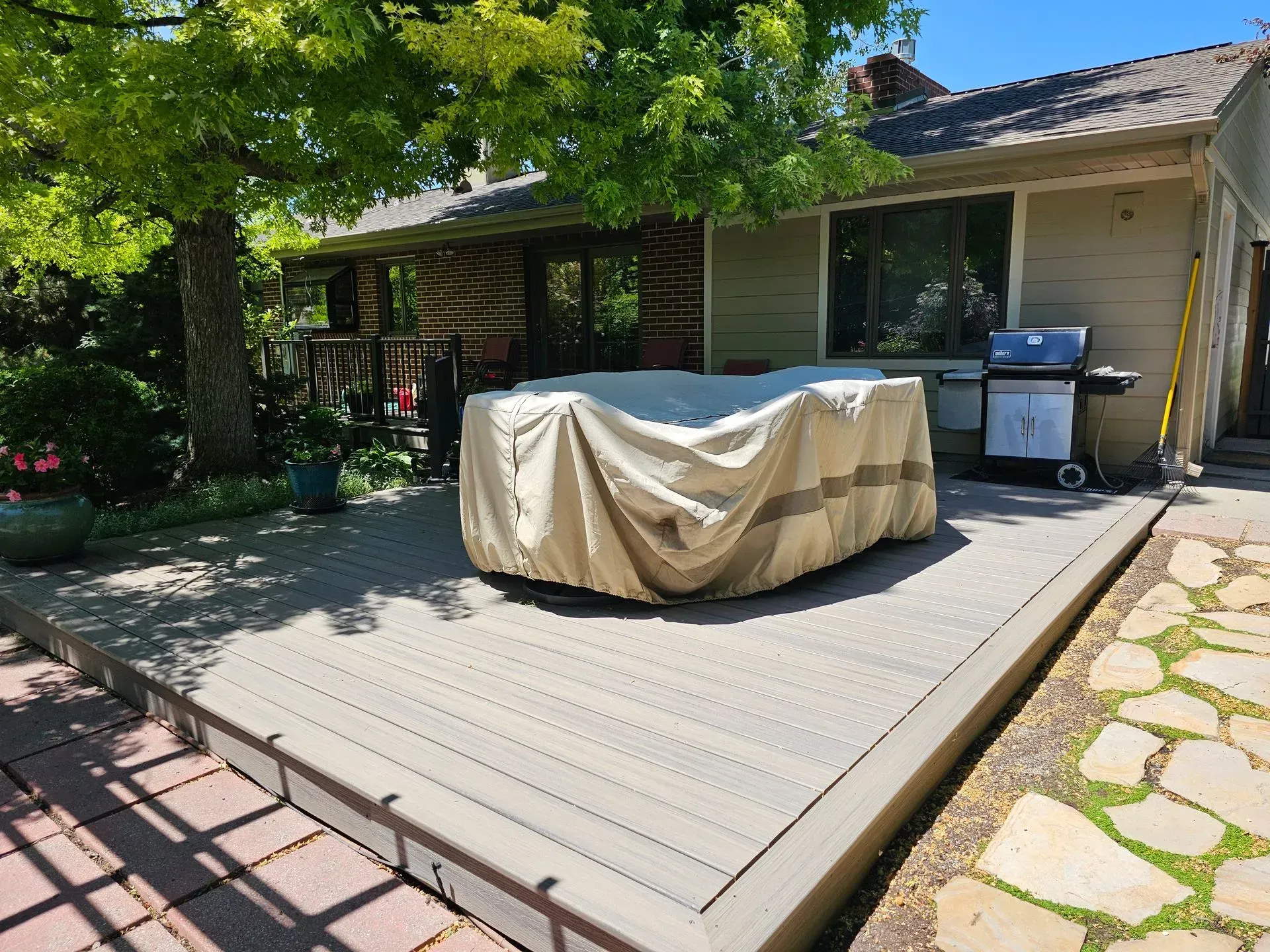 Backyard deck with a covered hot tub, grill, and stepping stones; sunny day.