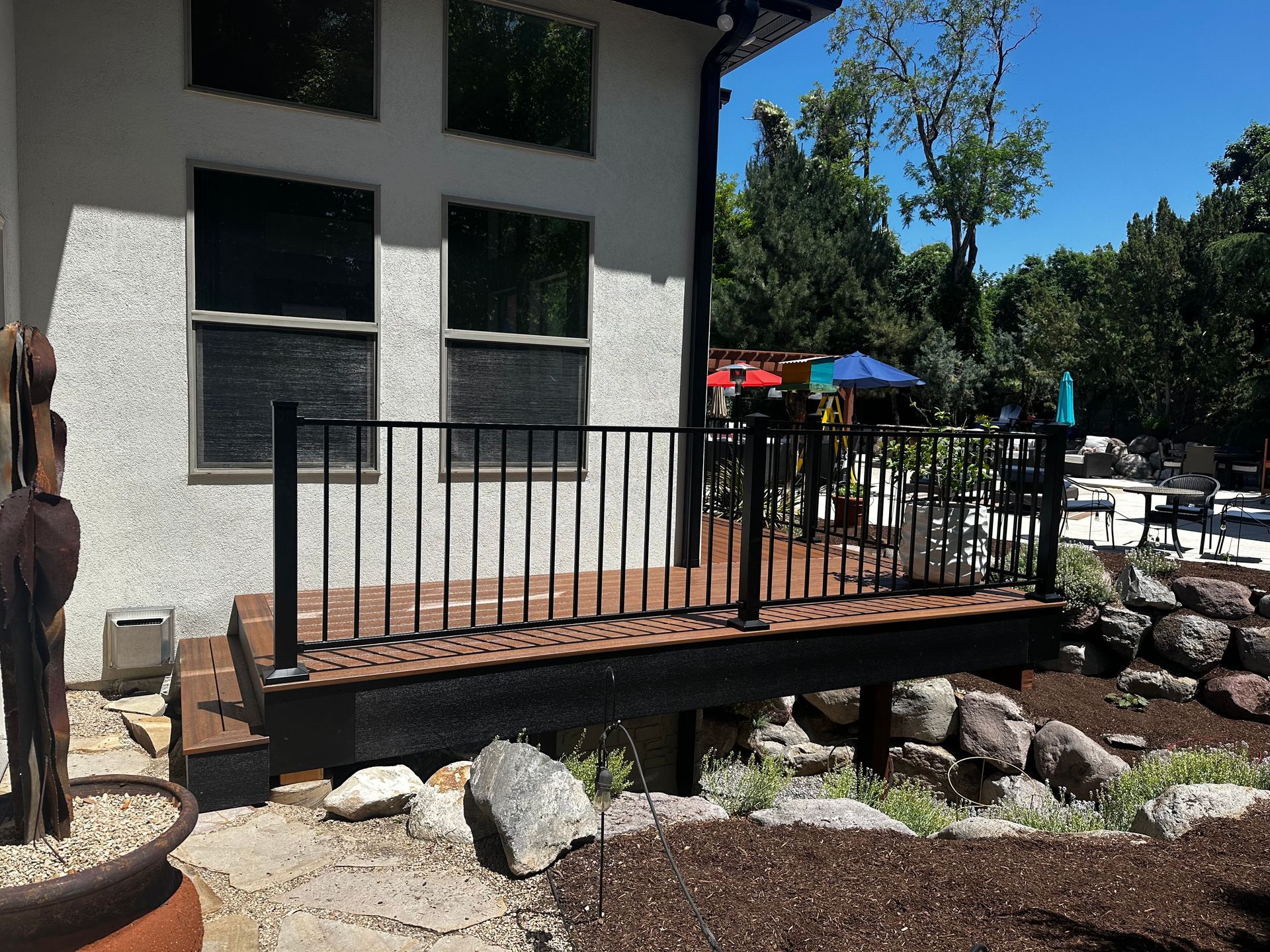 A deck with black railing outside a white house with windows, overlooking a pool area.