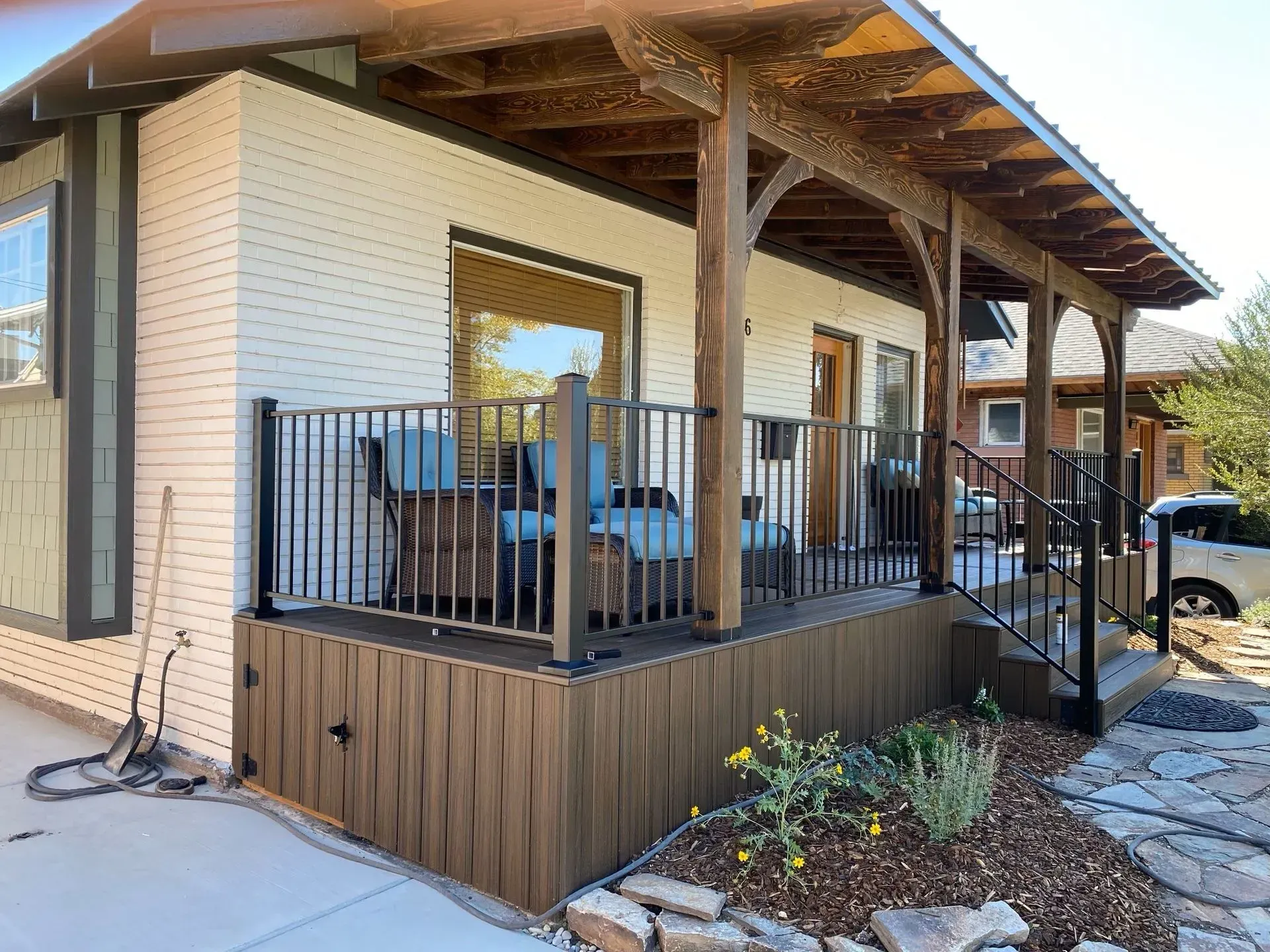 Brown deck with railing and seating on the porch of a white brick house.