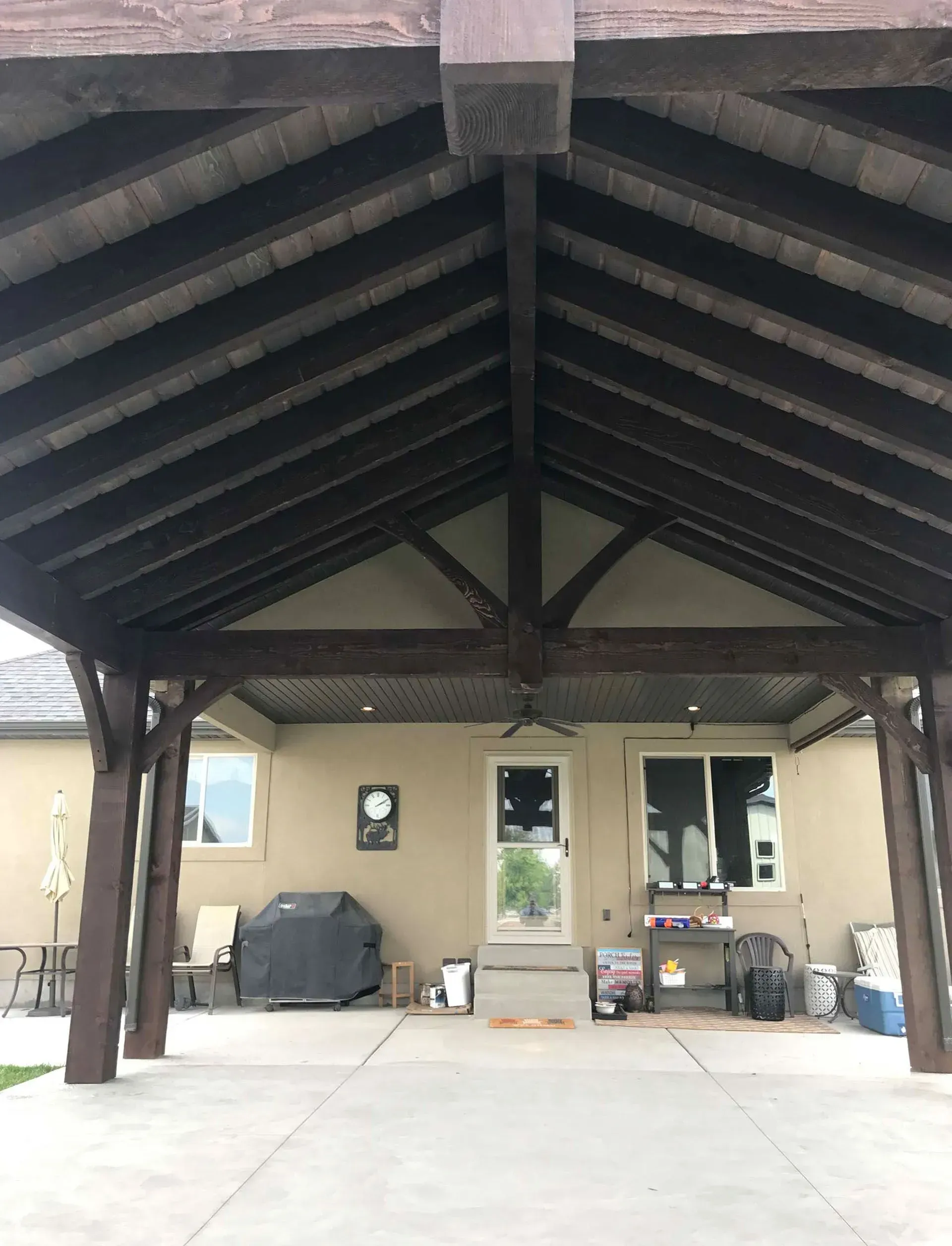 Covered outdoor patio with dark brown wooden beams and a concrete floor, backing onto a beige building.