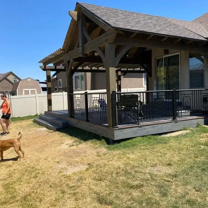 Wooden deck with pergola attached to a house, woman and dog in backyard.