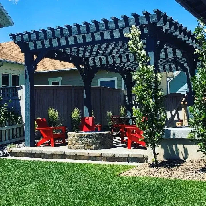 Black pergola over red chairs and fire pit on patio. Lush green lawn.