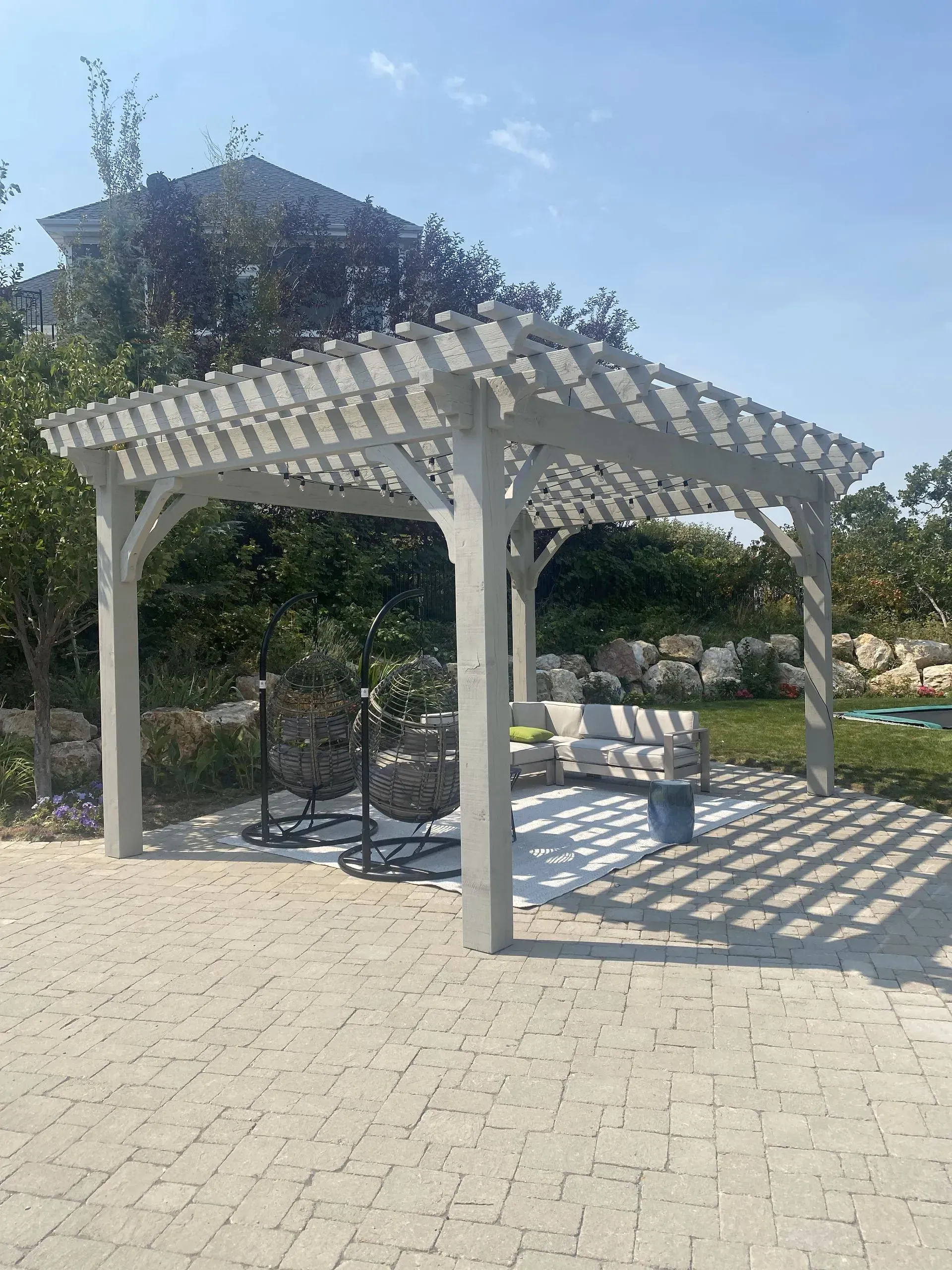 Grey pergola with a lattice roof casts shadows on a stone patio.
