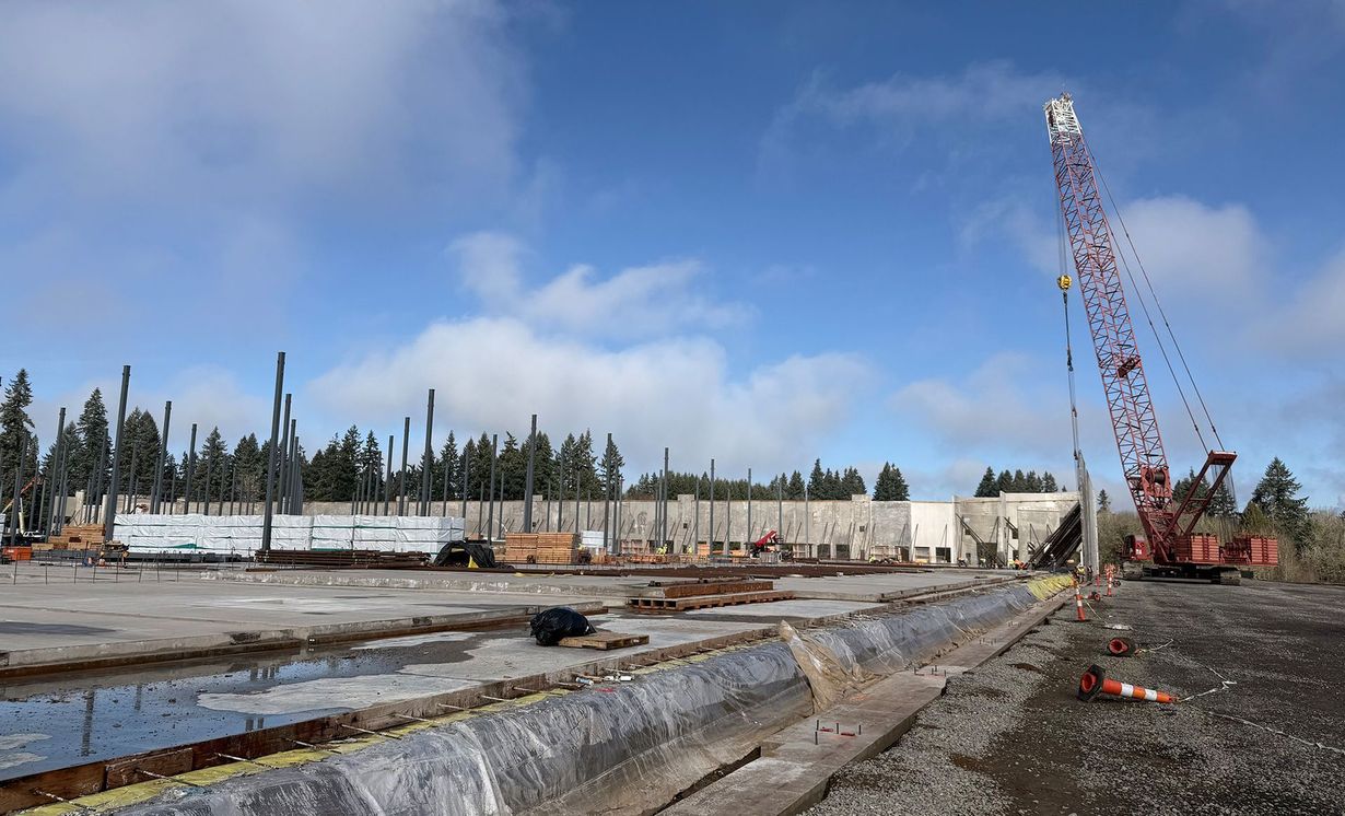 Construction site with cranes, concrete foundation, and long white buildings under a blue sky