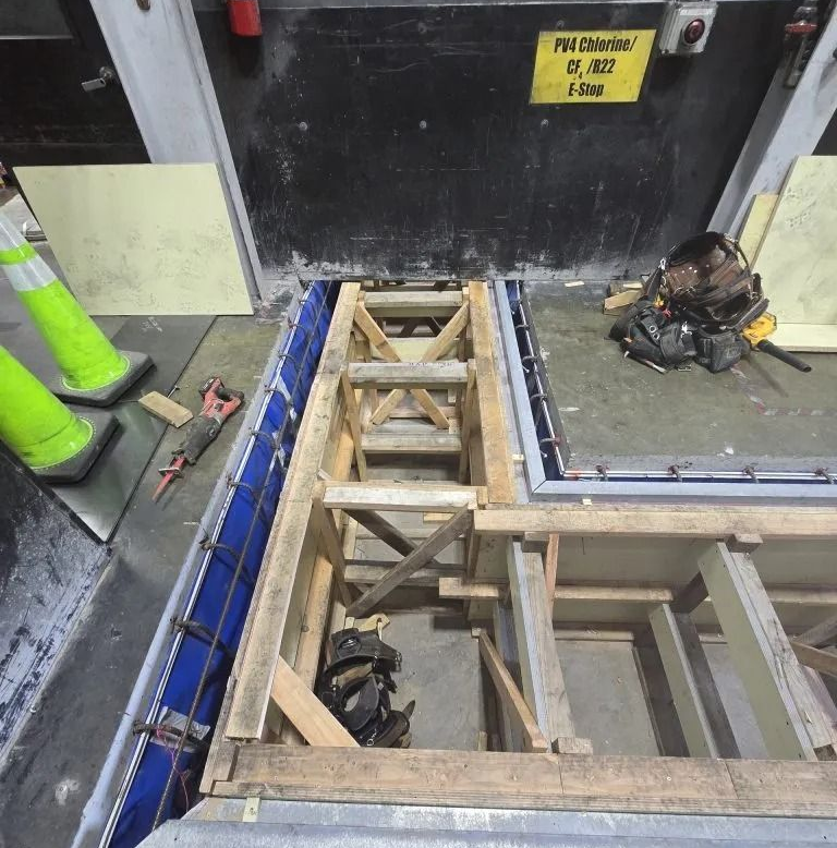 Construction opening with exposed wooden framing and blue panels beside a black wall, tools on the floor.