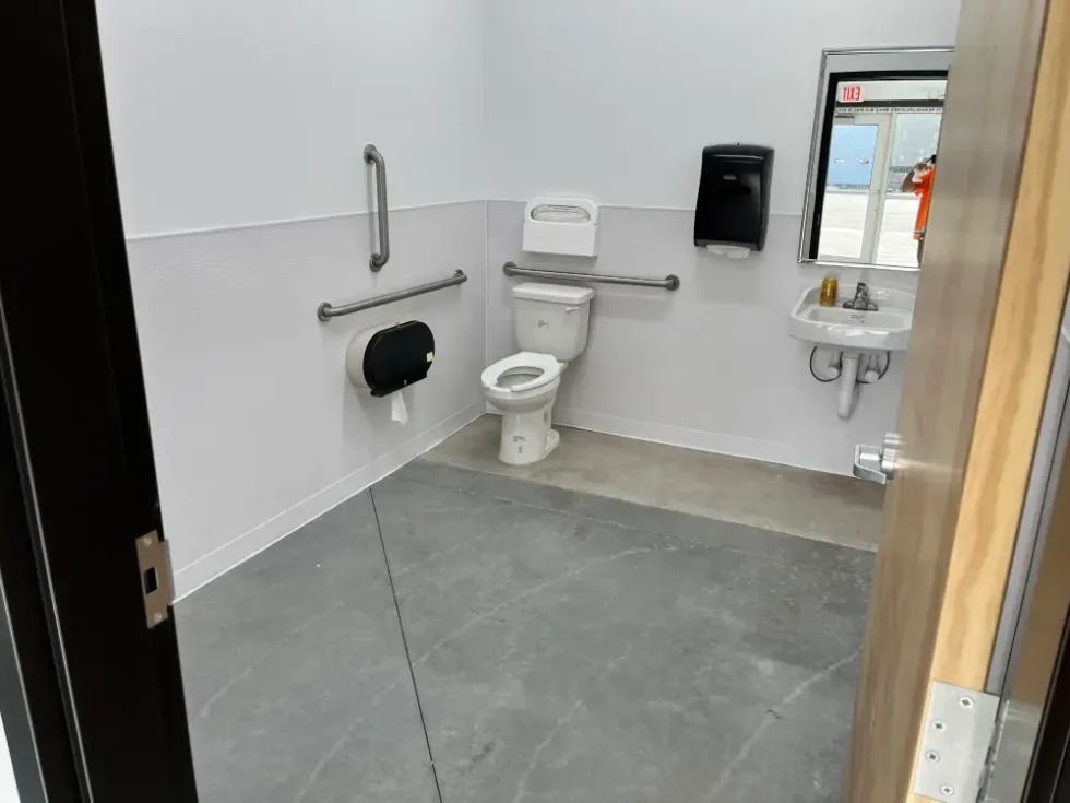 Accessible public restroom featuring a toilet with grab bars, a sink, and a paper towel dispenser on white walls.