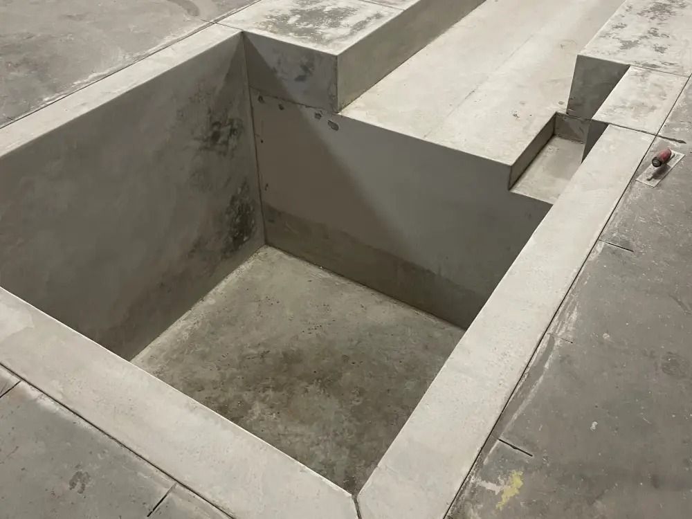 A square concrete pit recessed into a floor, featuring stepped edges and a small adjacent cutout in the corner.
