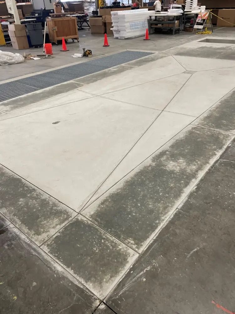 Newly poured concrete flooring with a diamond-shaped section delineated by saw cuts inside a warehouse setting.