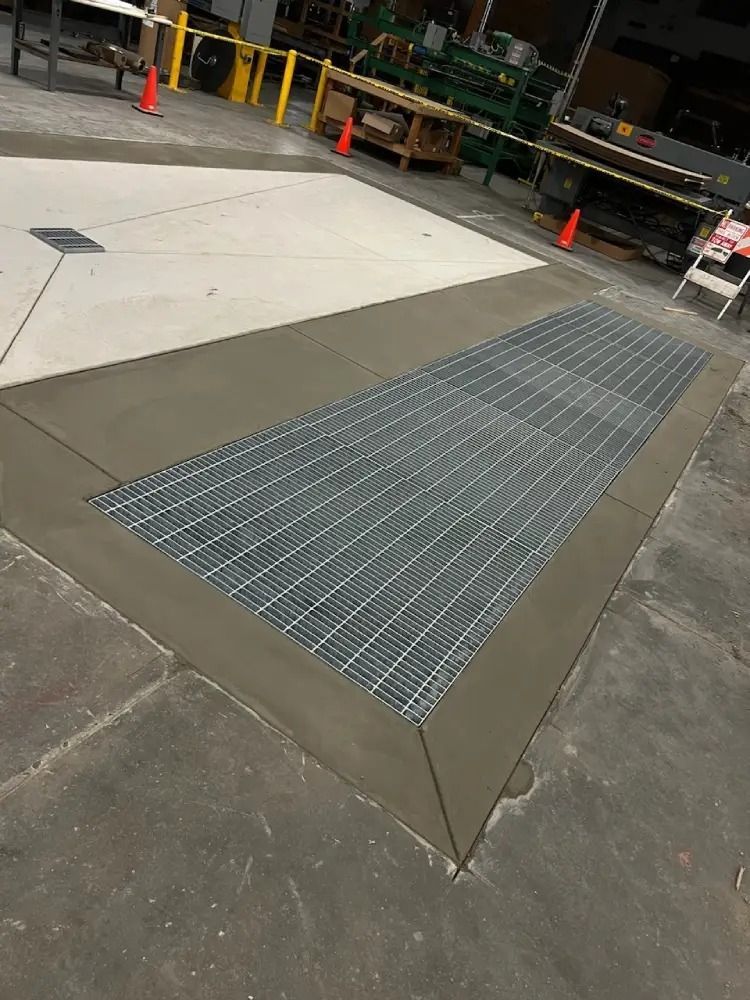 A concrete industrial floor with a rectangular metal trench grate surrounded by a smooth, finished concrete border.