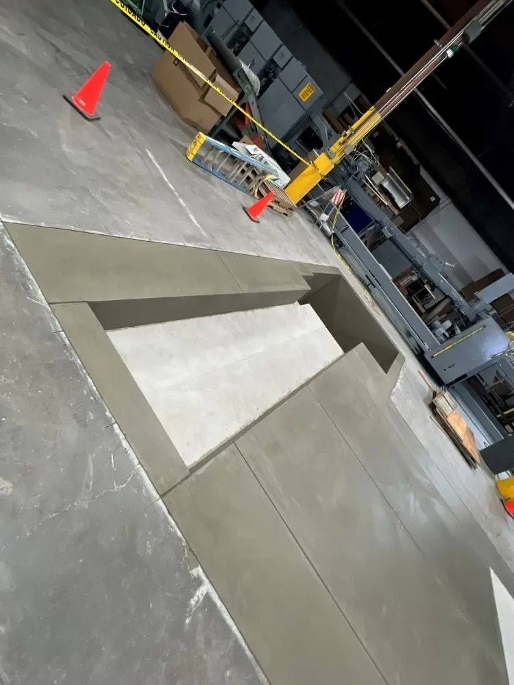 A rectangular concrete trench cut into a gray indoor industrial floor, with orange traffic cones marking the perimeter.