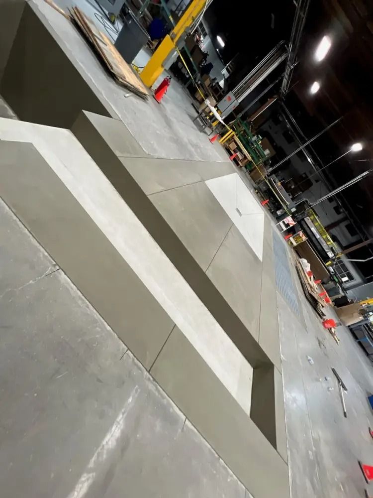 A rectangular concrete form or trench in a dimly lit warehouse with a yellow support post in the background.