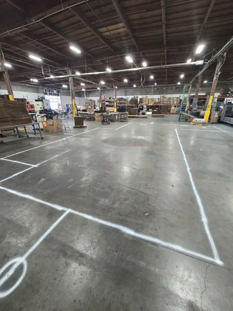 A spacious, dimly lit warehouse with concrete floors marked by white paint outlines for designated floor zones.