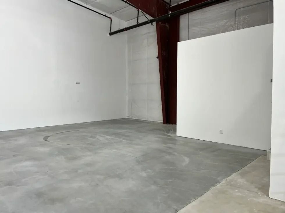 An interior view of an unfinished commercial space with white walls, a concrete floor, and a dark support beam.