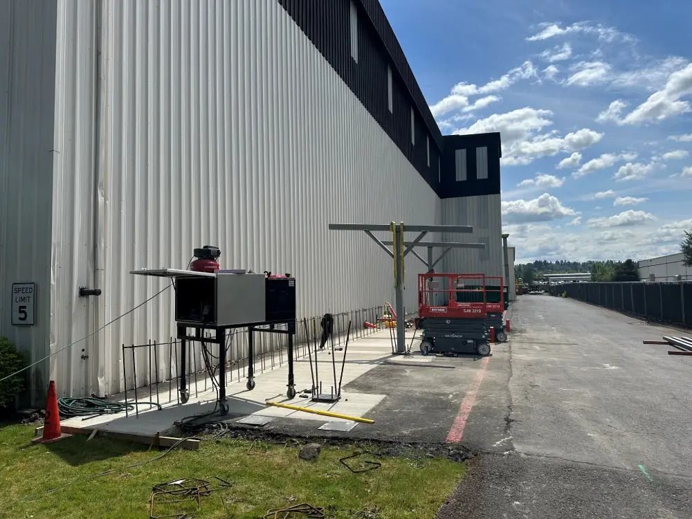 An exterior view of a commercial building with white metal siding, featuring construction equipment and tools nearby.