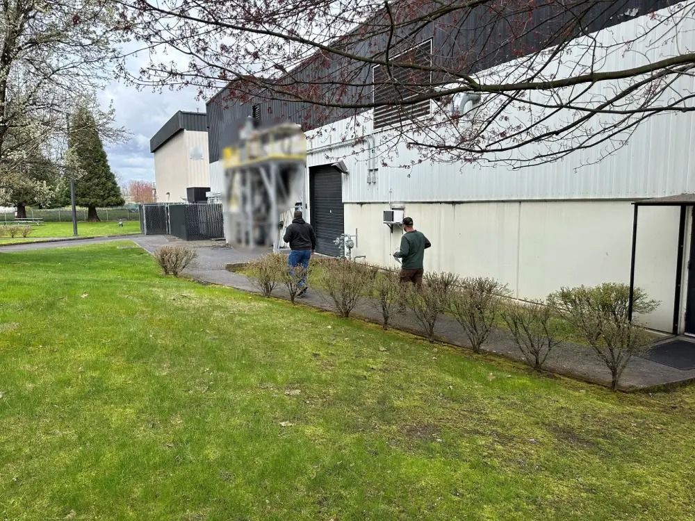 Two people walk along a paved path next to a building and a lawn on a cloudy day.