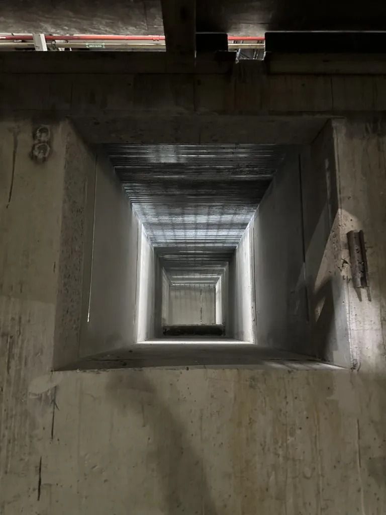 A narrow, rectangular concrete tunnel or shaft viewed head-on, receding into a light-filled opening in the distance.