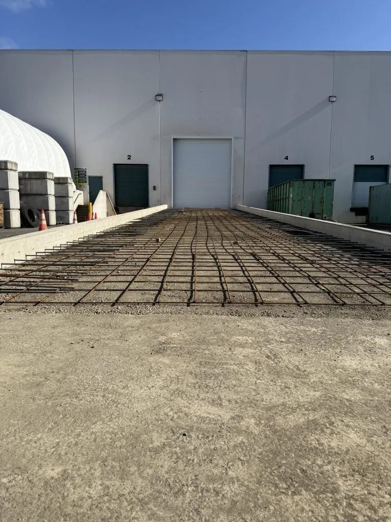 A steel rebar grid laid on a concrete surface leading to a warehouse loading dock.