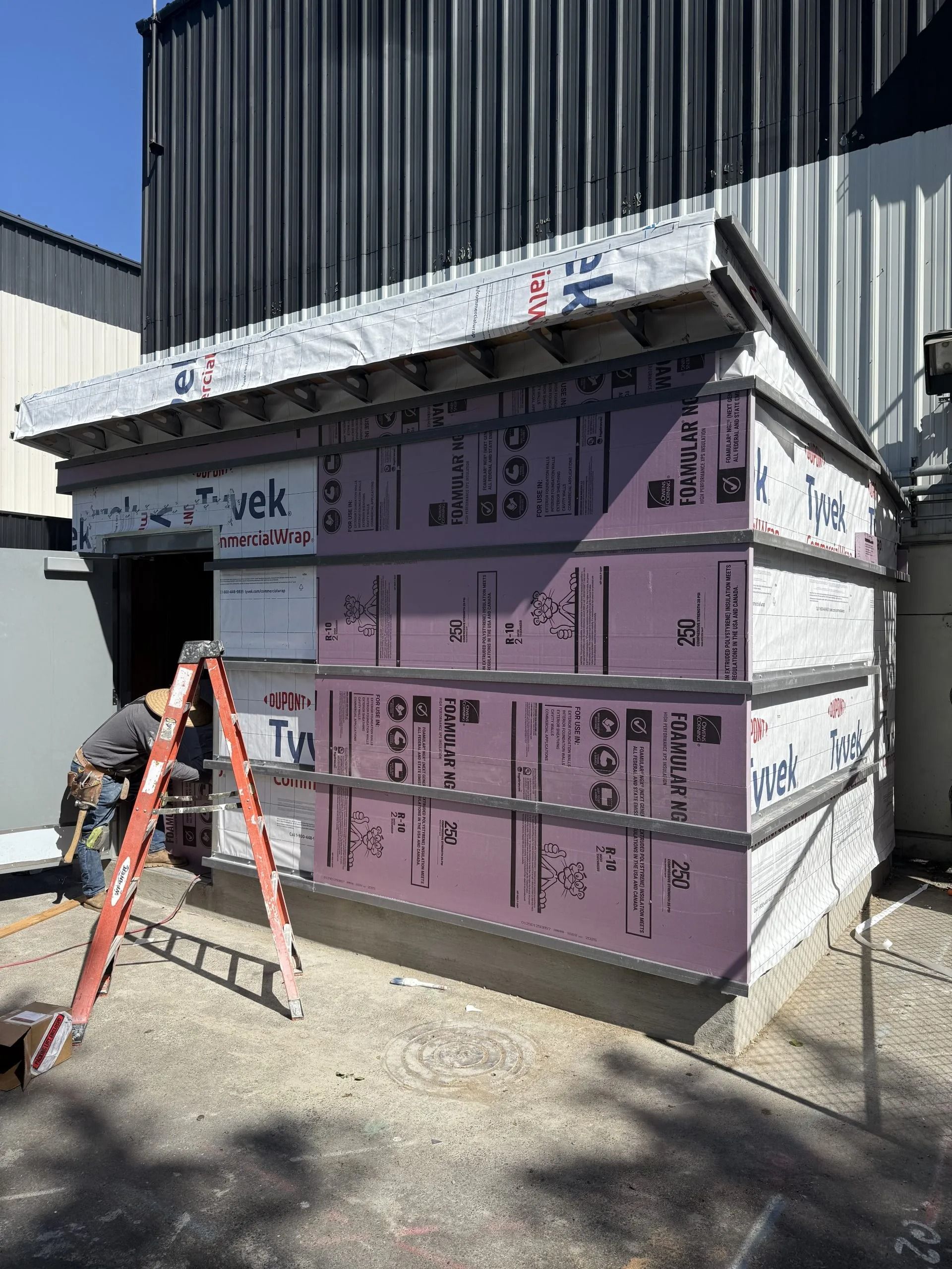 A construction worker on a ladder installs siding panels on the exterior wall of a building.