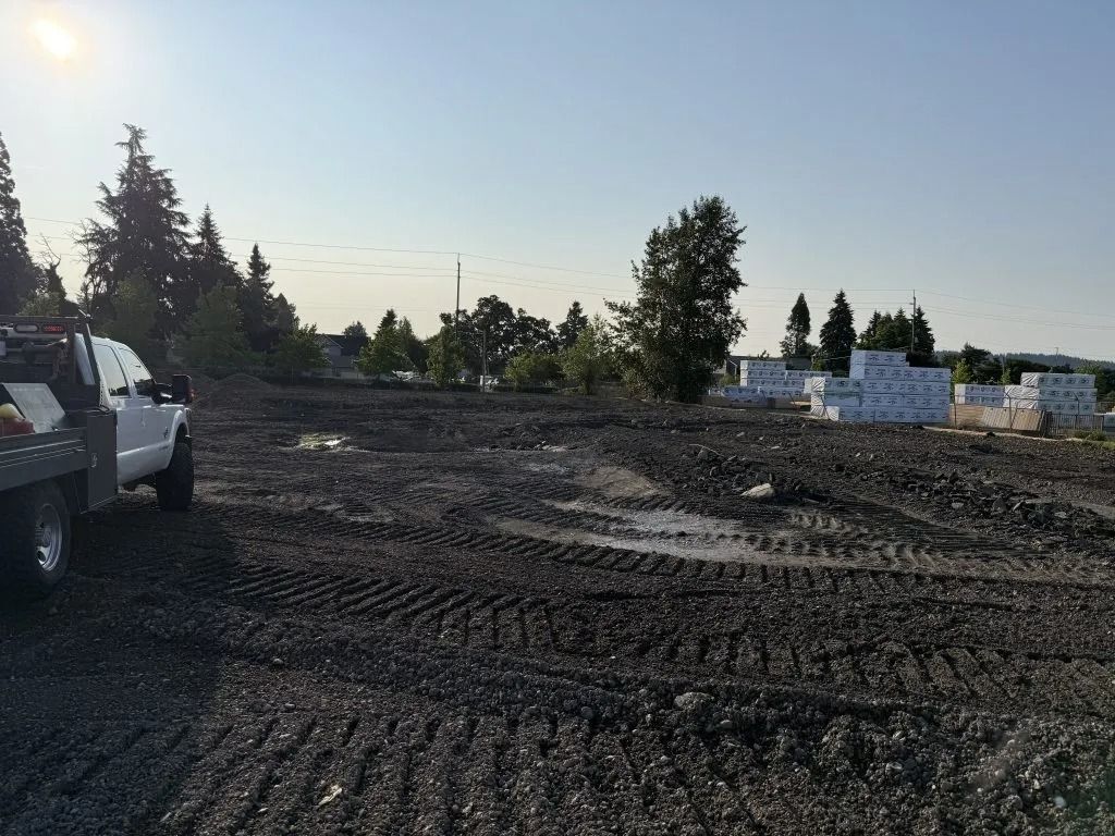 A white work truck parked on a muddy, tire-tracked construction site with white building materials stacked in the distance.