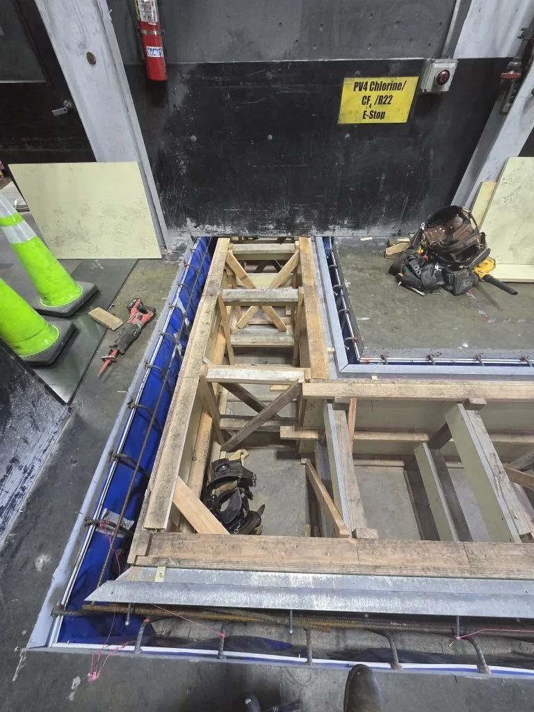 A construction site featuring wooden concrete forms with metal reinforcement bars in a rectangular, indoor work area.