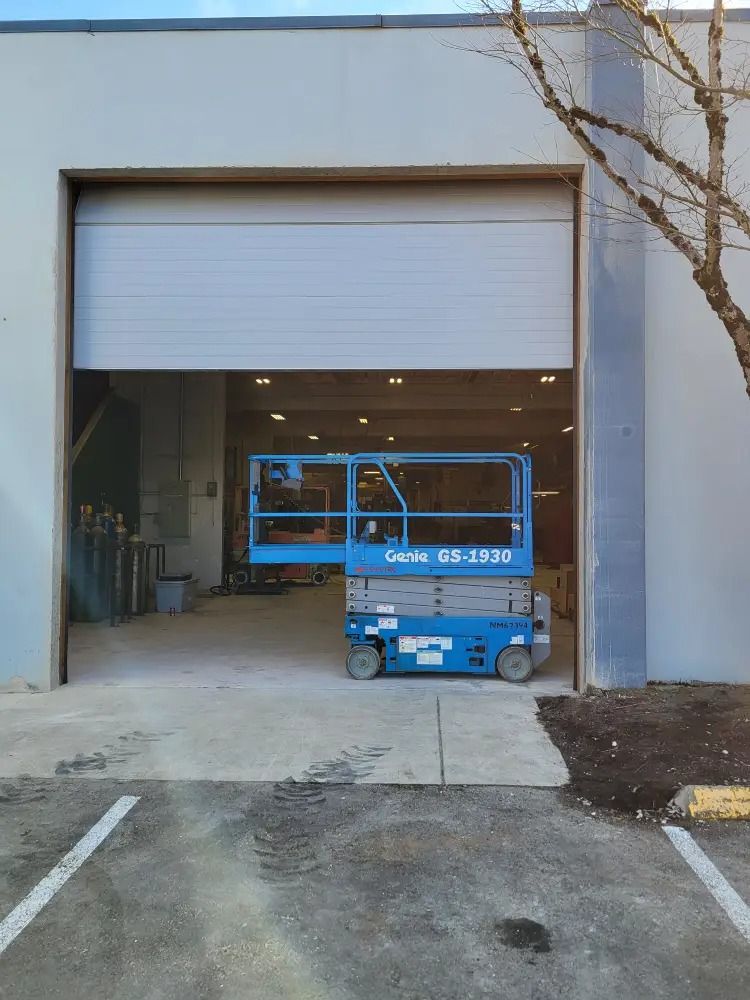 A blue Genie GS-3232 scissor lift parked inside a large, open warehouse bay.