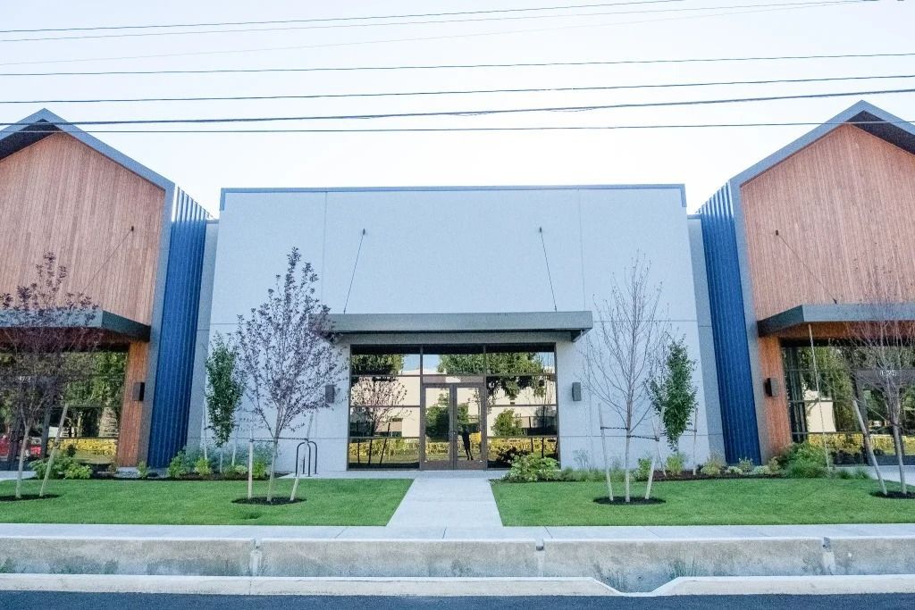 Modern single-story office building with gray walls, wood-paneled gable wings, and a glass-paneled entrance.