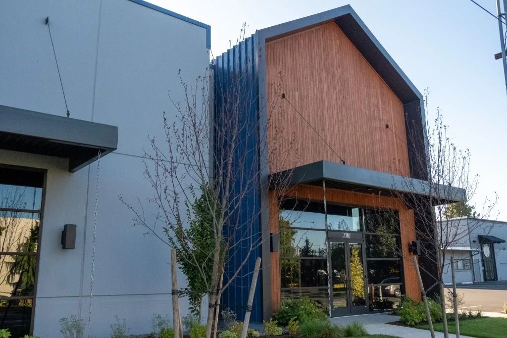 Modern commercial building with a blue metal facade, a wood-paneled gable entrance, and glass windows under a sunny sky.