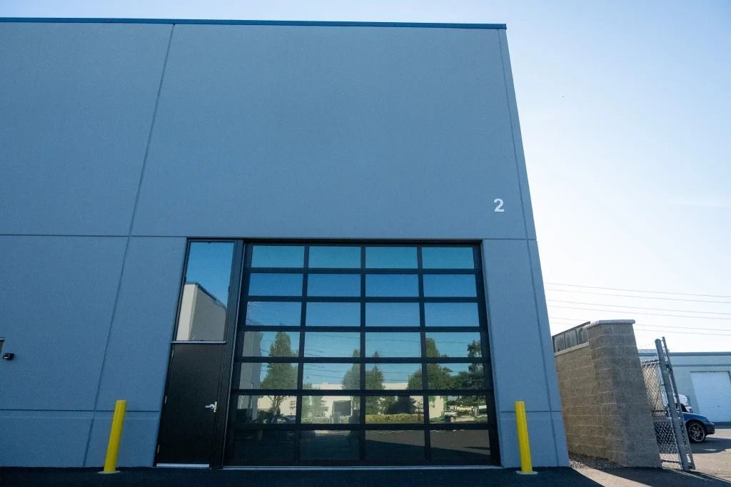 A blue commercial building with a black pedestrian door and a large, multi-pane glass sectional garage door.
