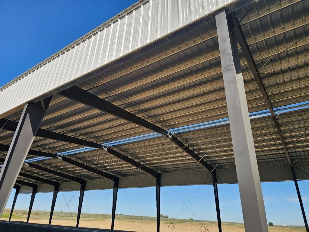 Low-angle view of a large, open-air metal warehouse structure with dark steel columns and a corrugated metal roof.