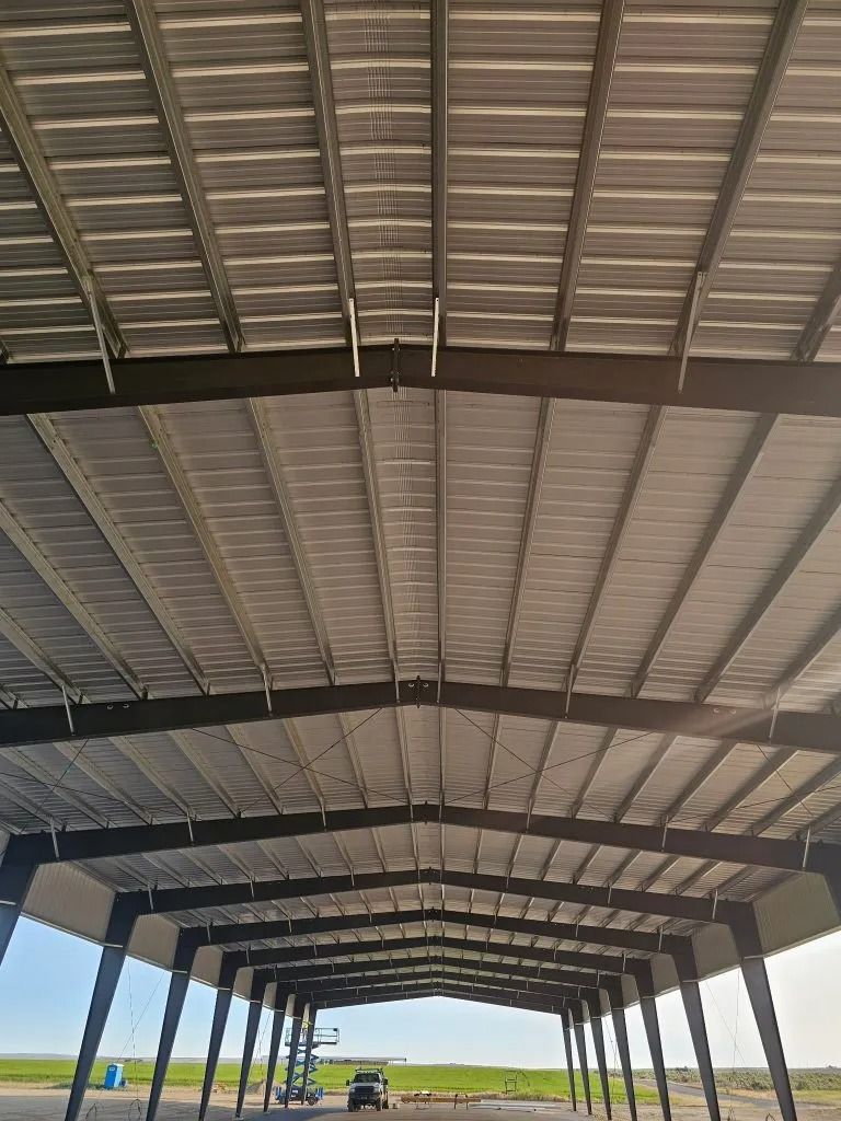 Interior view of an open-sided steel warehouse with a corrugated metal roof and exposed dark structural beams.