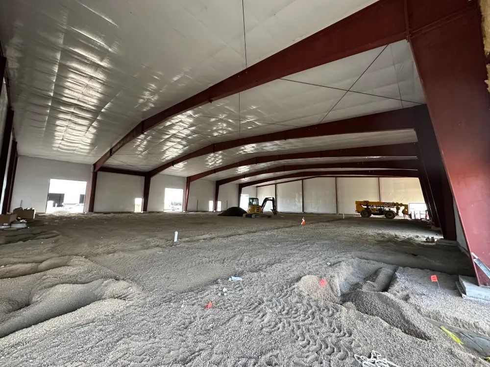 Interior view of a large, empty commercial building under construction with exposed steel beams and a gravel floor.