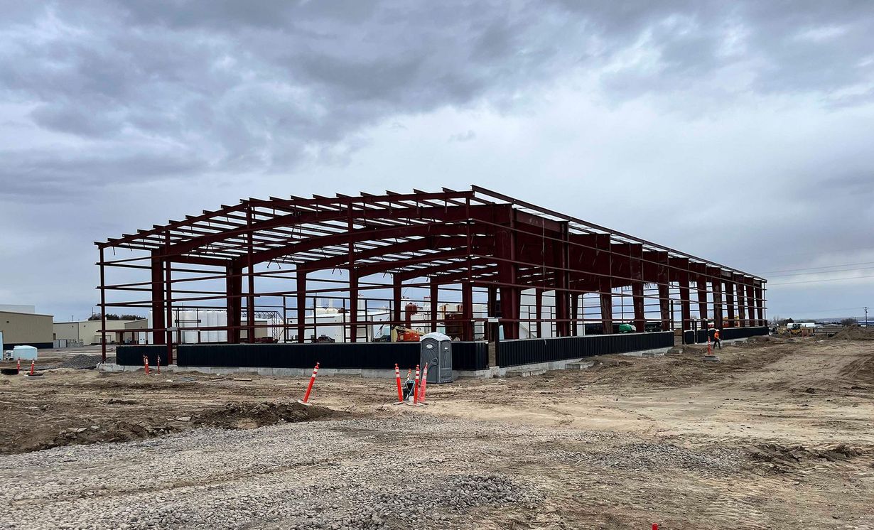 Partially built steel warehouse frame on a dirt lot under a cloudy sky