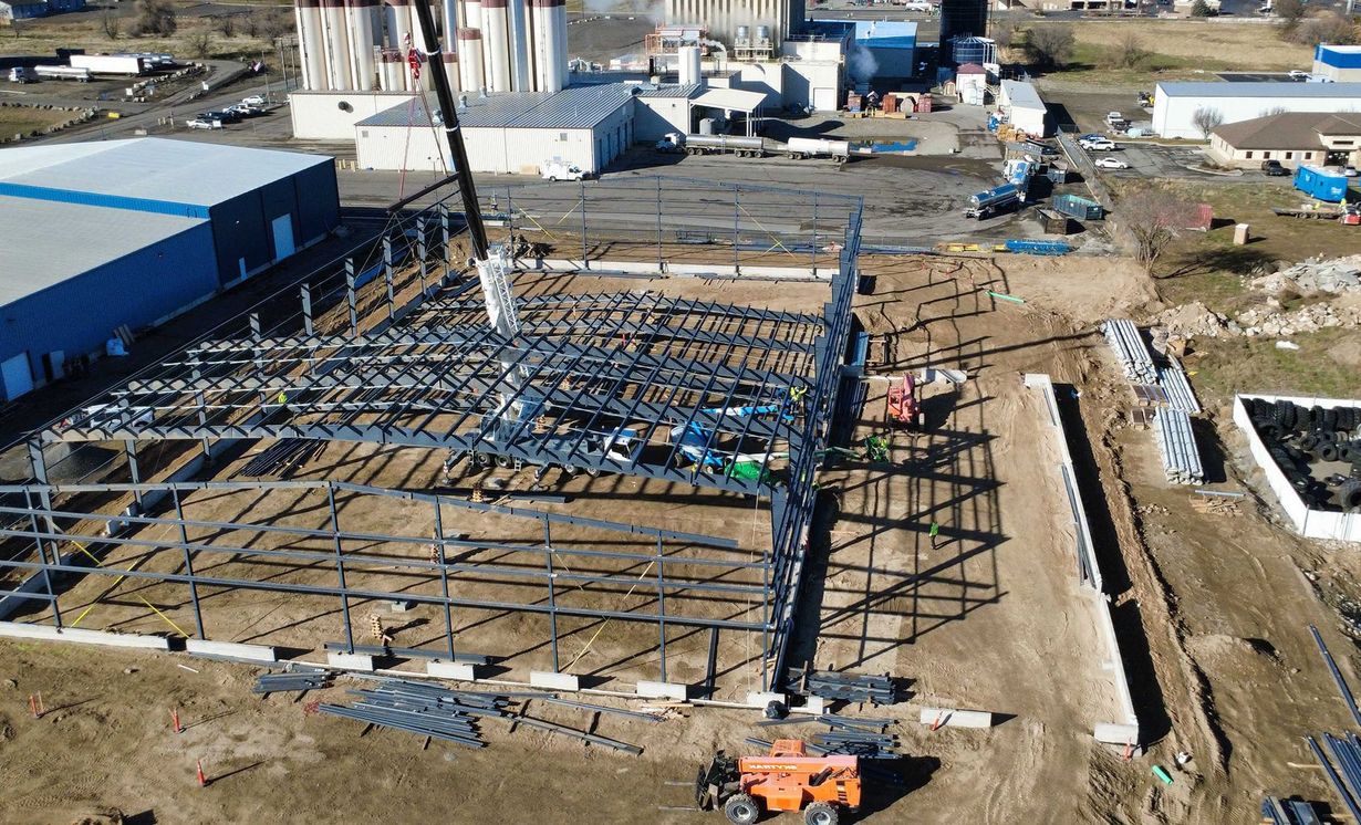 Aerial view of a steel frame building under construction with workers and machinery on a muddy site